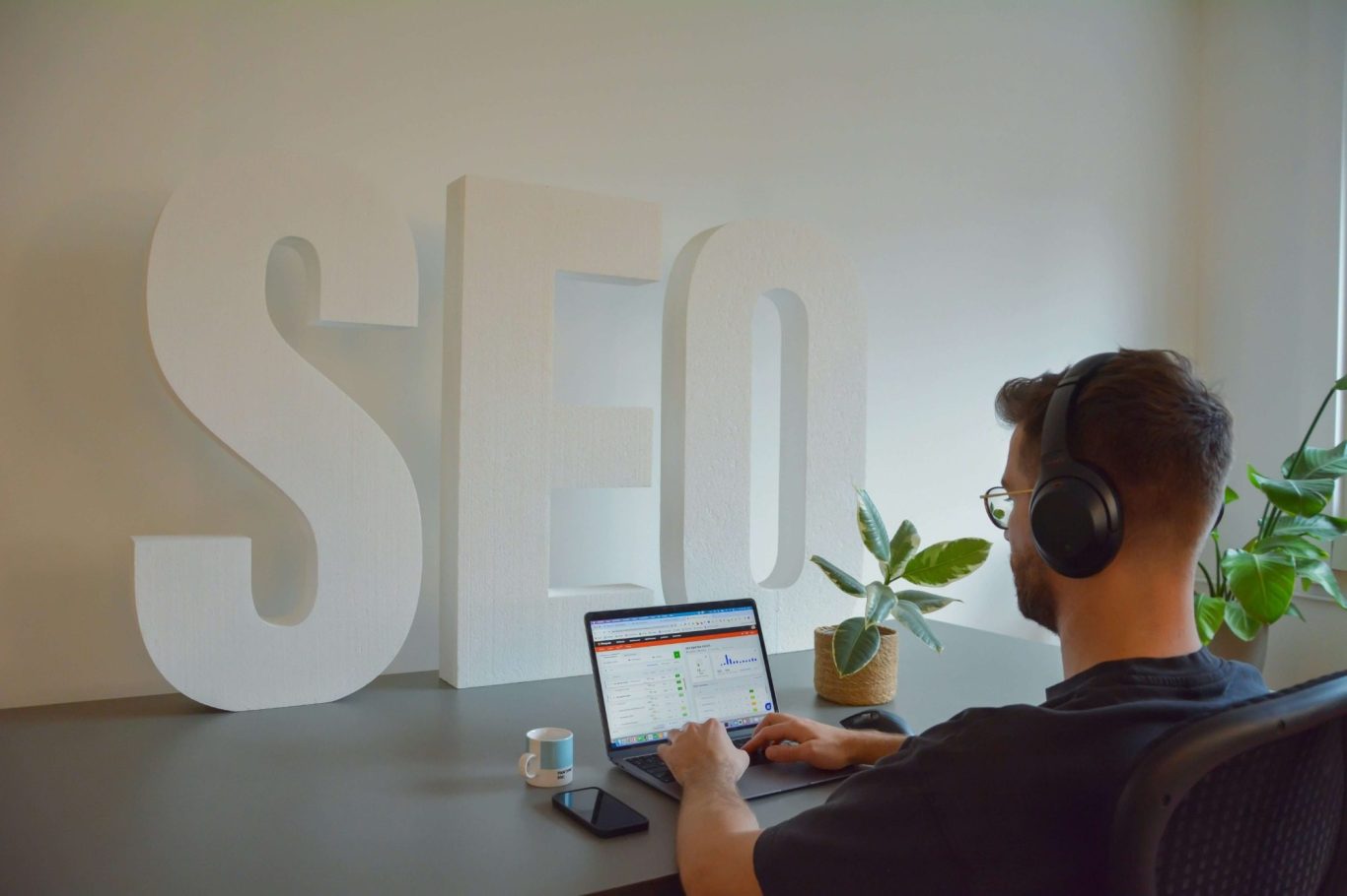 My Story and Mission Person wearing headphones working on a laptop with a large "SEO" sign in the background.